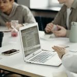 Working on laptop at table with other people conducting a microsoft CRM audit can optimise systems